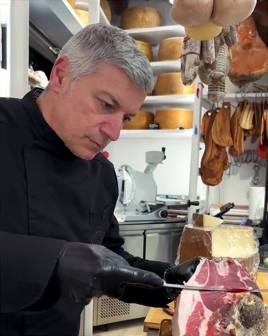 Paolo Taccalite affetta un pezzo di coppa al banco, tra i prosciutti e le forme di formaggio della bottega