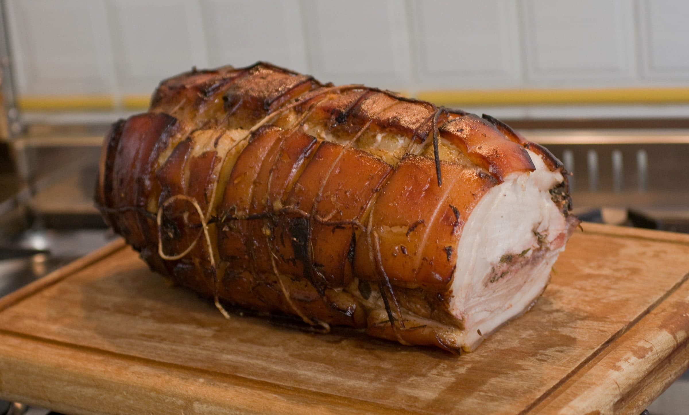 Porchetta intera legata sul tagliere, la crosta dorata e il taglio che scopre la carne