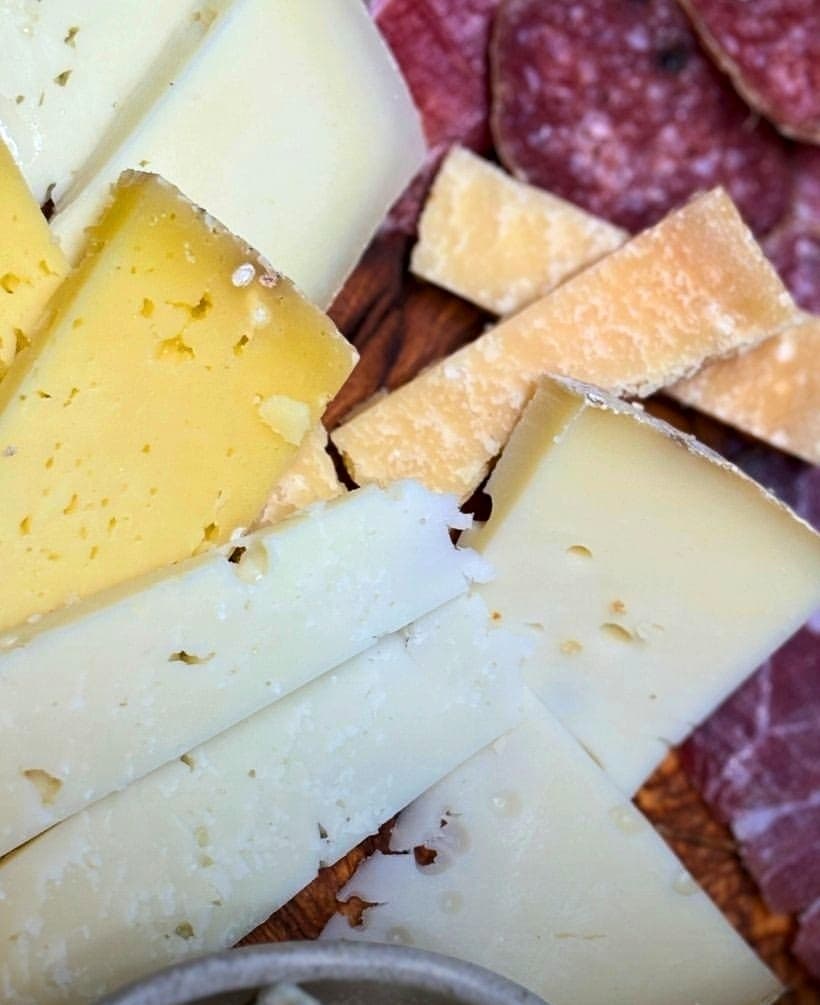 Formaggi al taglio sul tagliere di legno, accanto ai salumi affettati